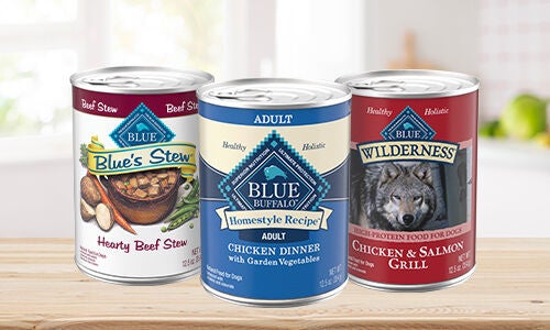 Three cans of wet Blue Buffalo dog food on a wood counter